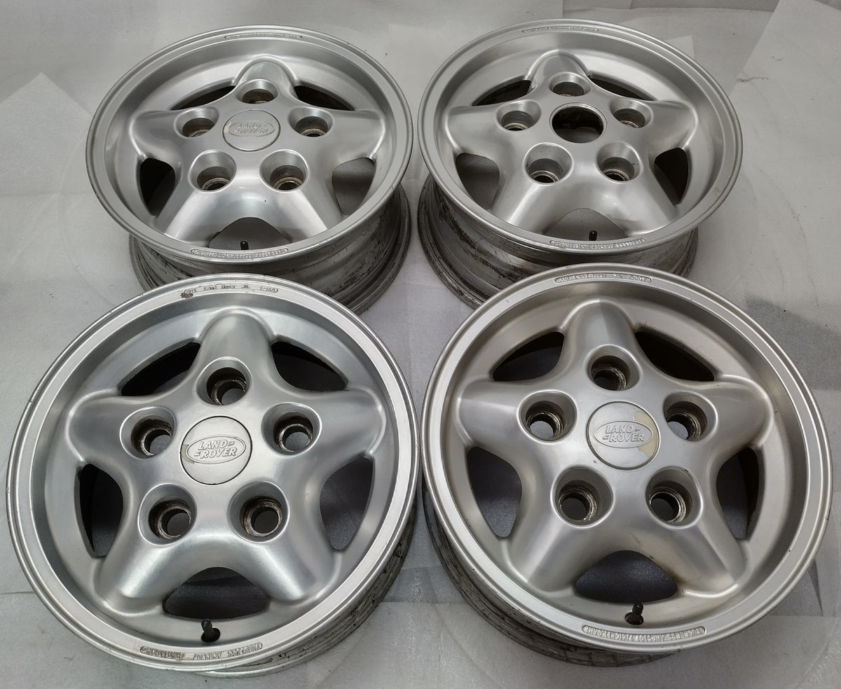 “Set of four used silver Land Rover OEM five-spoke wheels with three center caps and visible rim wear.”

