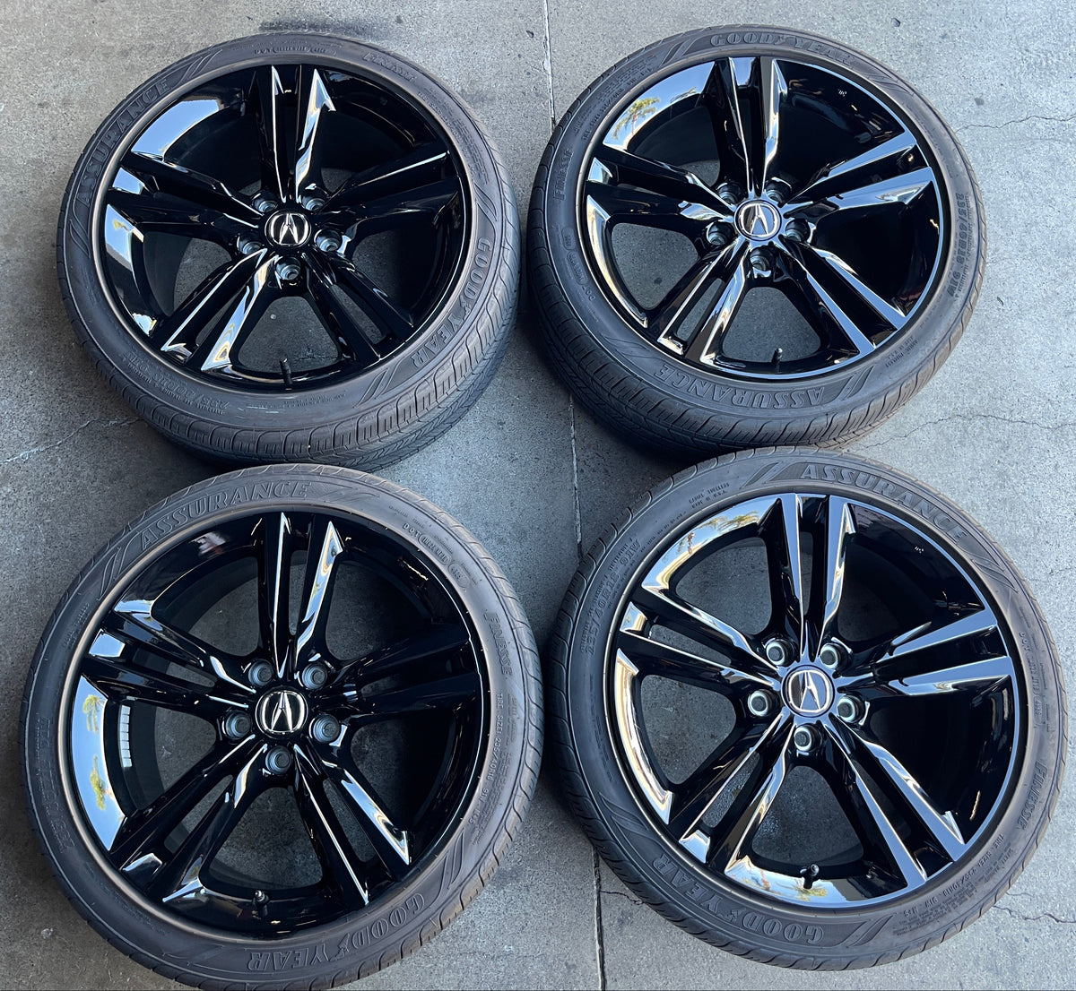 Four gloss black Acura Integra OEM wheels with Goodyear Assurance tires and Acura center ca