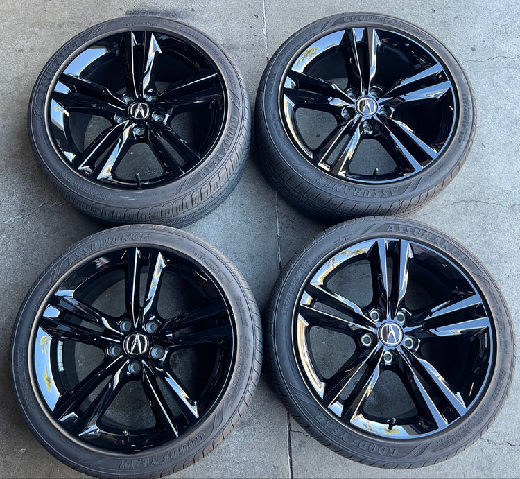 Four gloss black Acura Integra OEM wheels with Goodyear Assurance tires and Acura center ca