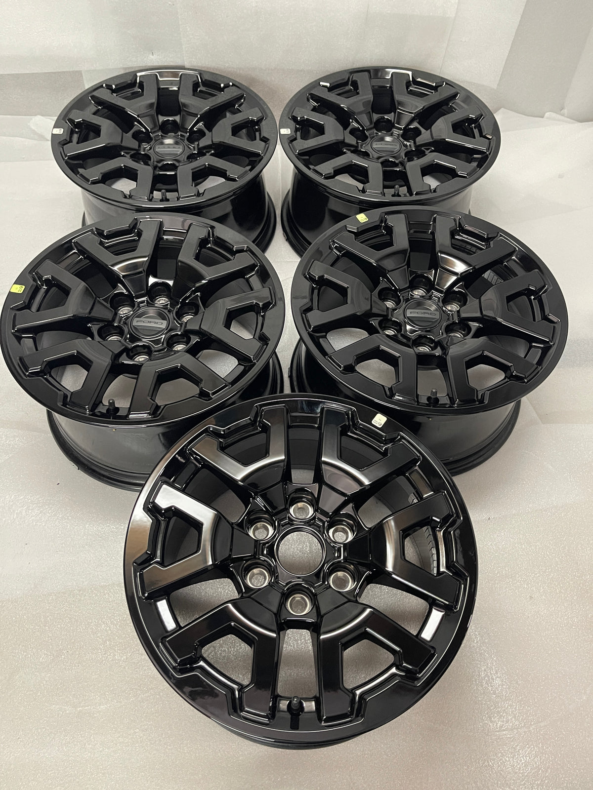 Five gloss-black Ford OEM 17-inch wheels arranged in rows, with four Ford center caps and one uncapped wheel in front.
