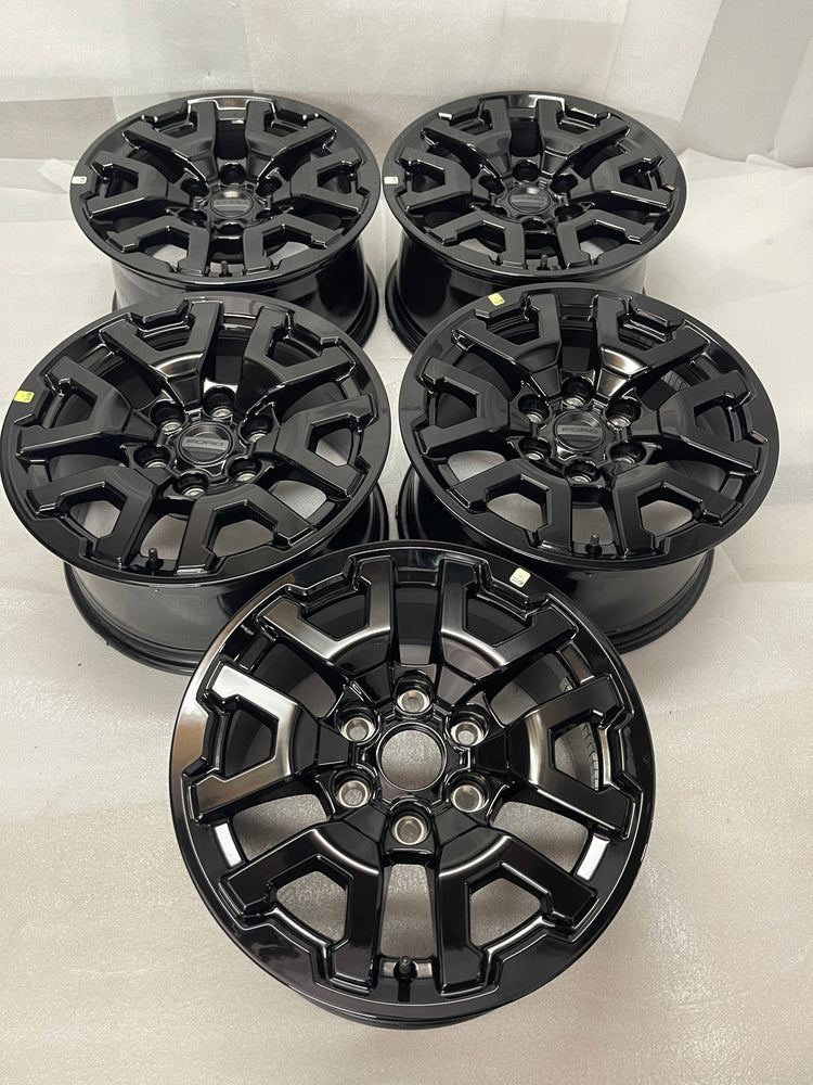 Five gloss-black Ford OEM 17-inch wheels arranged in rows, with four Ford center caps and one uncapped wheel in front.